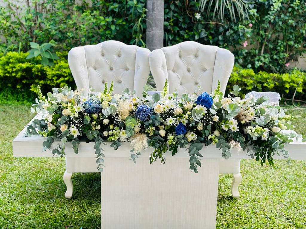 Mesa de novios blanca con sillas capitonadas y arreglo floral azul y blanco